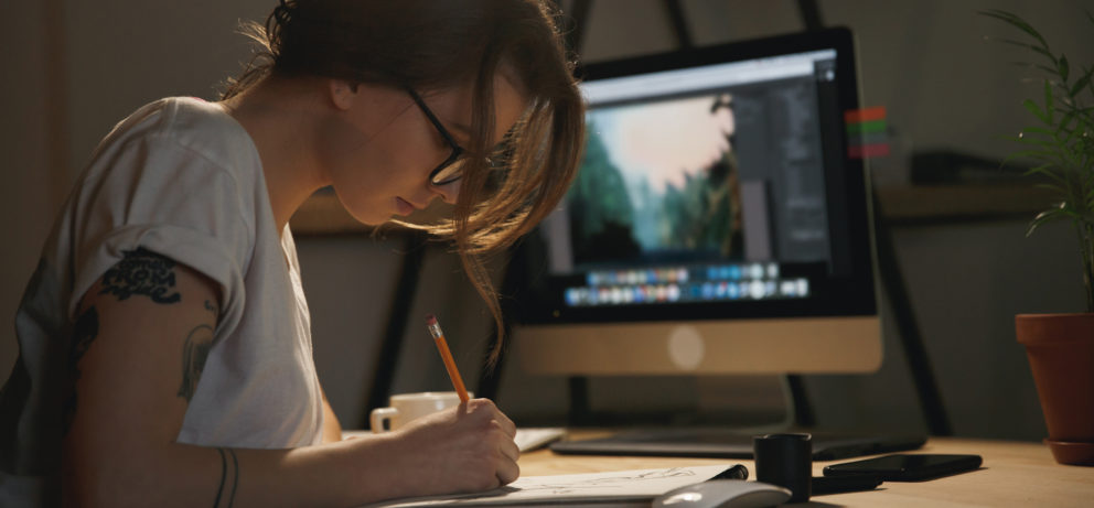 Young woman designer sitting indoors at night drawing sketches